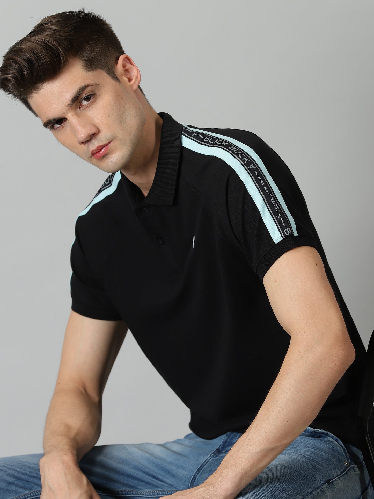 Man wearing a black polo shirt with light blue stripes on a gray background